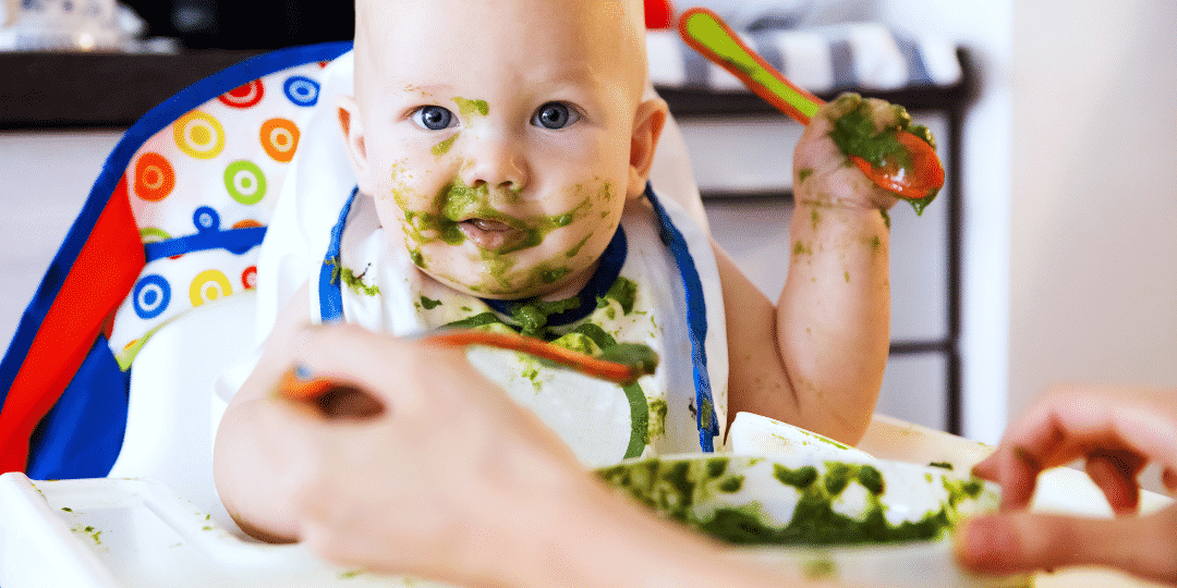 parent introduce solids to baby with green puree on face