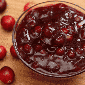 bowl of cranberry sauce with cranberries on the table in the background