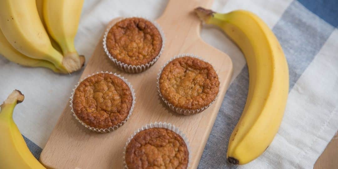 baby friendly banana oat muffin with bananas on the side served on a cutting board