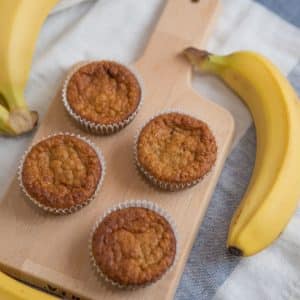 baby friendly banana oat muffin with bananas on the side on a cutting board
