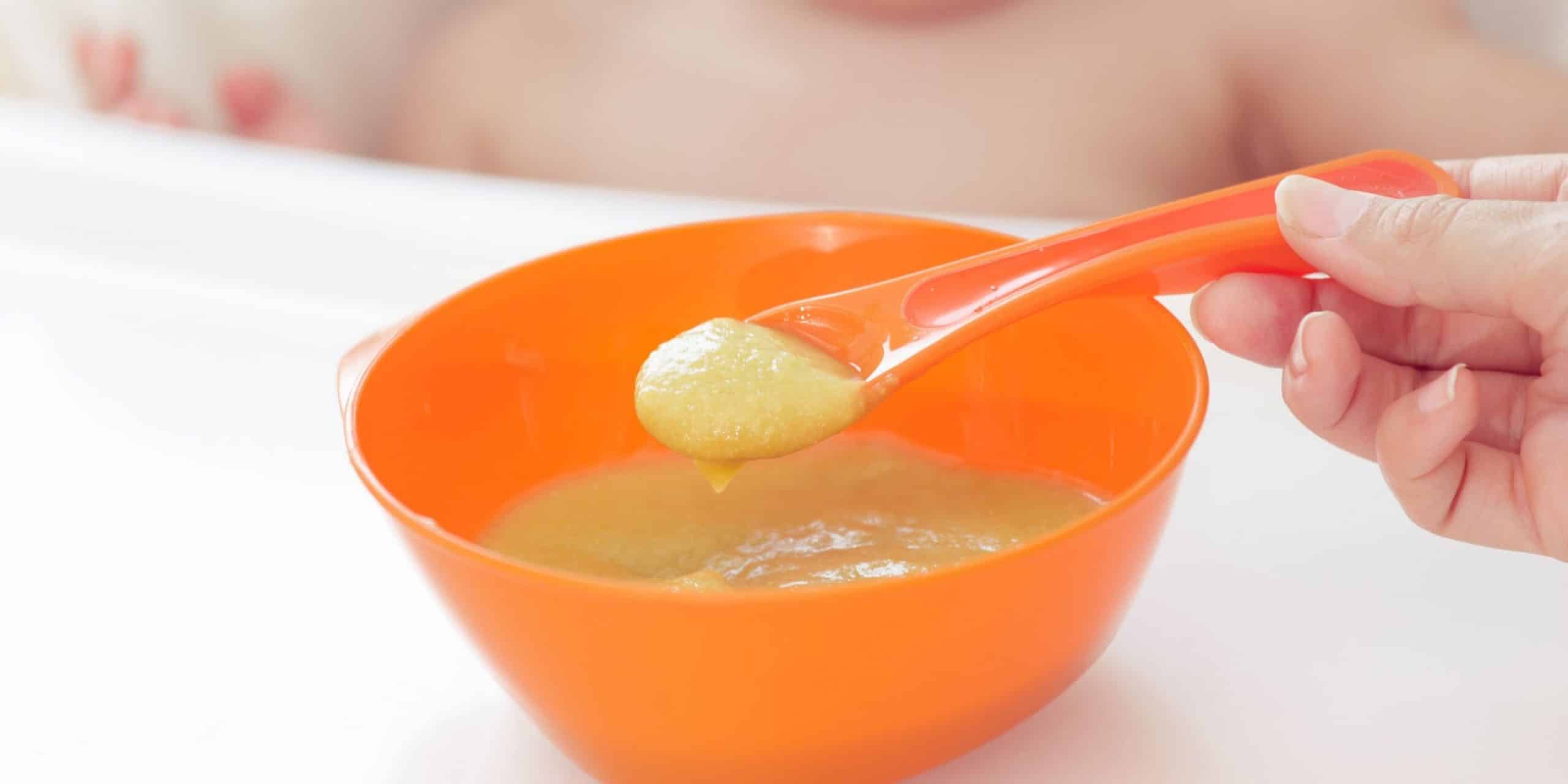 bowl of puree baby food with spoon and baby