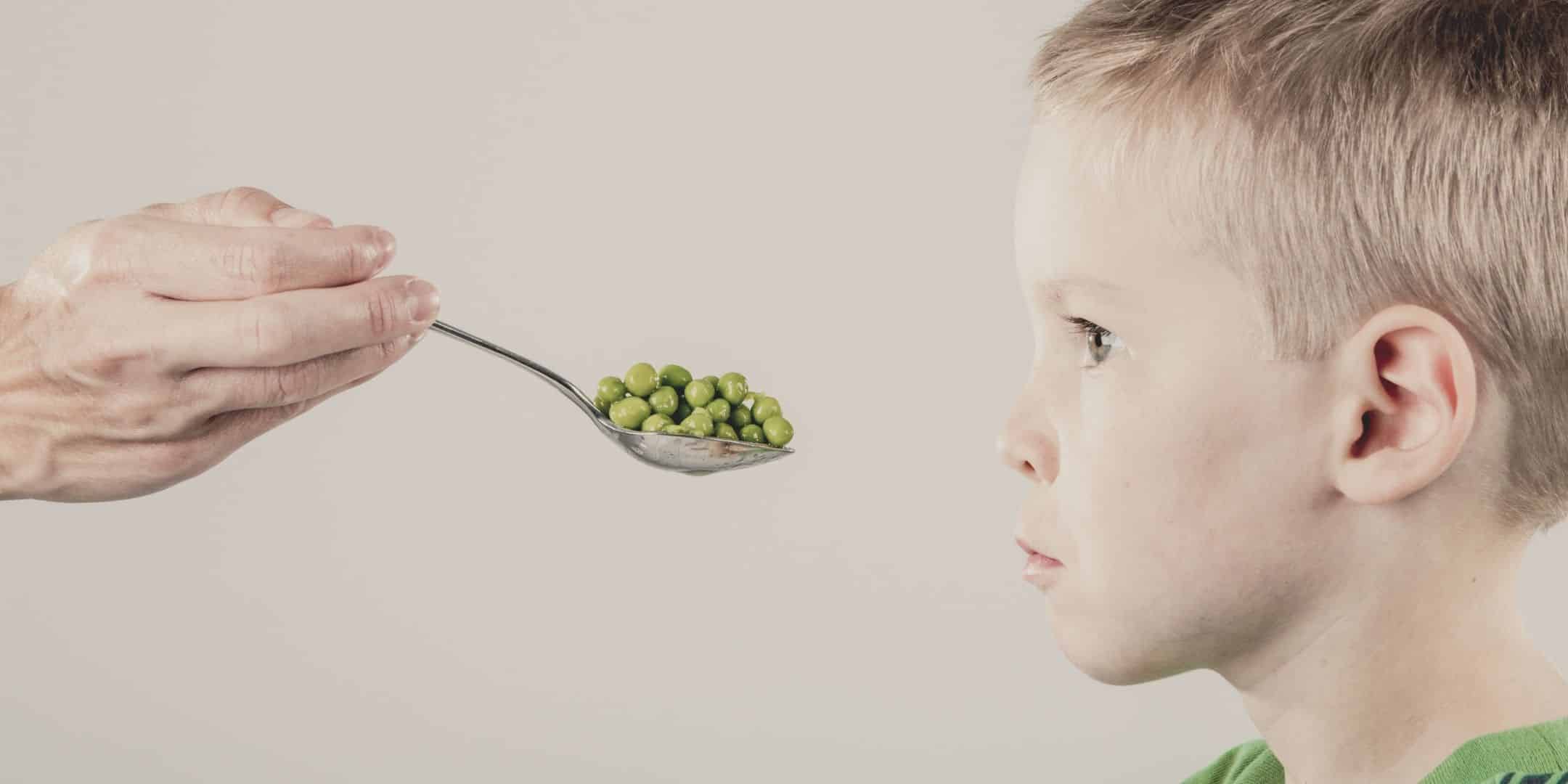 hand feeding peas to a picky eater child with mouth closed