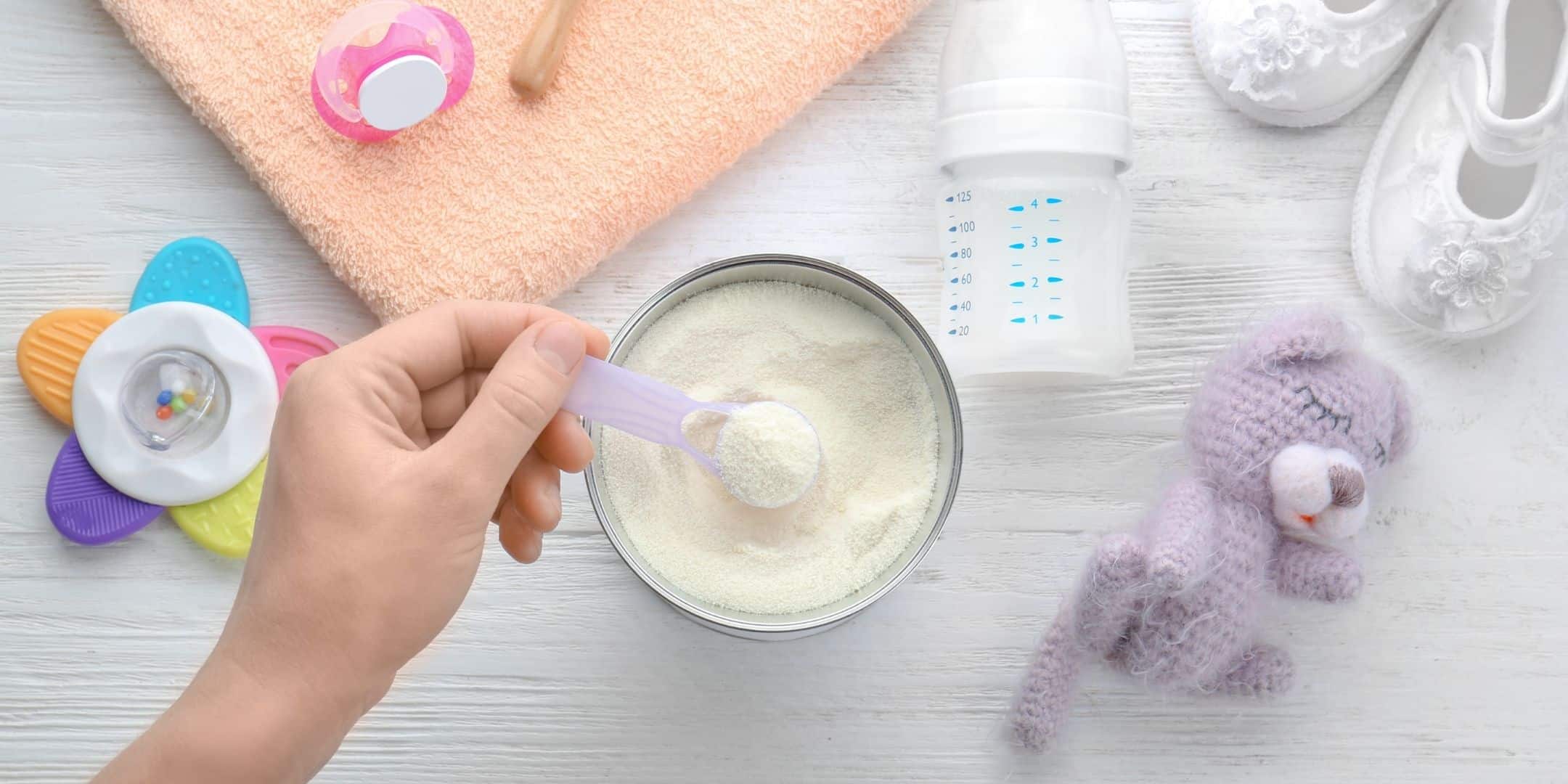 infant formula can and scoop with bottle and baby toys around it