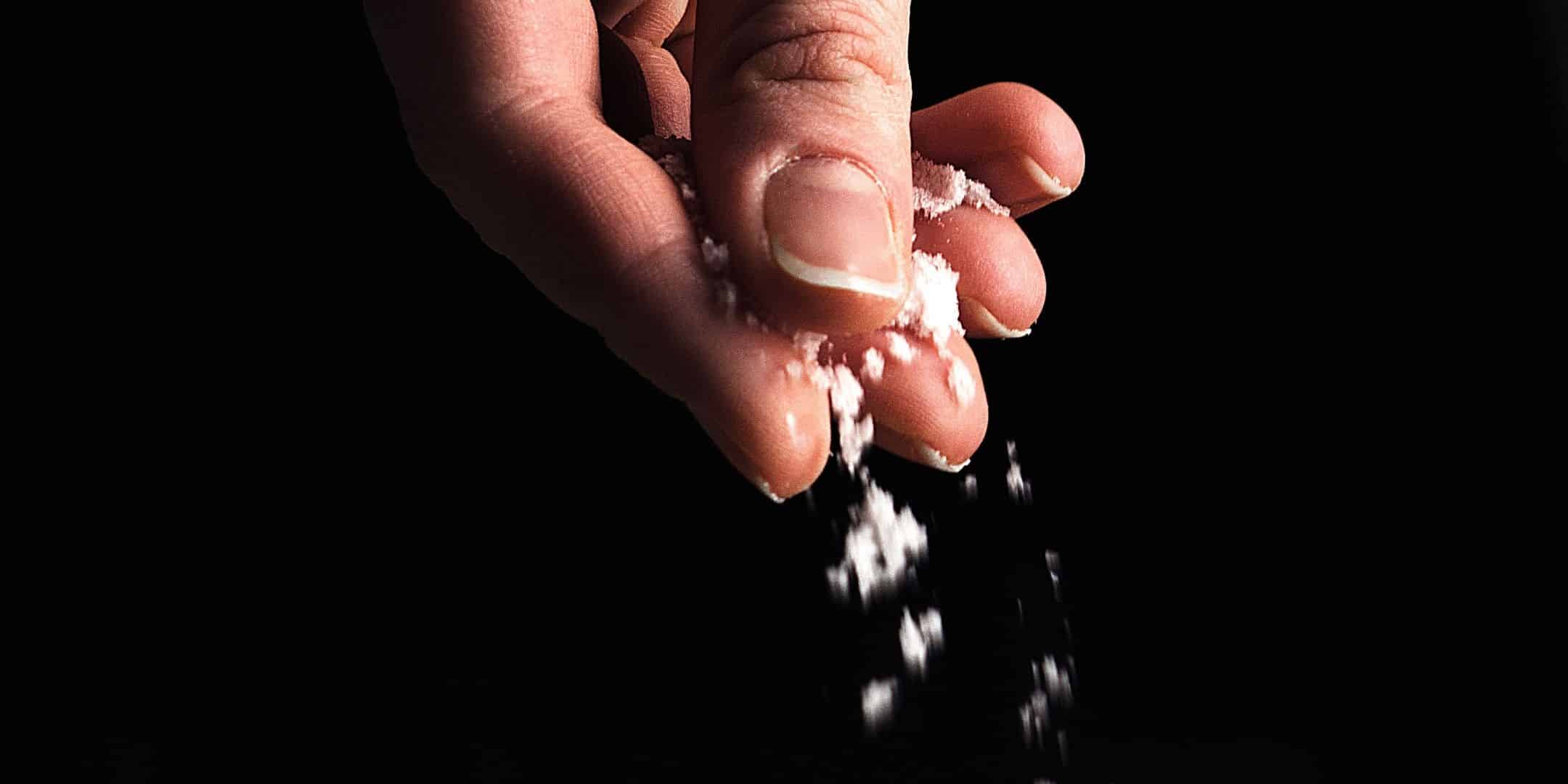 hand sprinkling salt over a black background