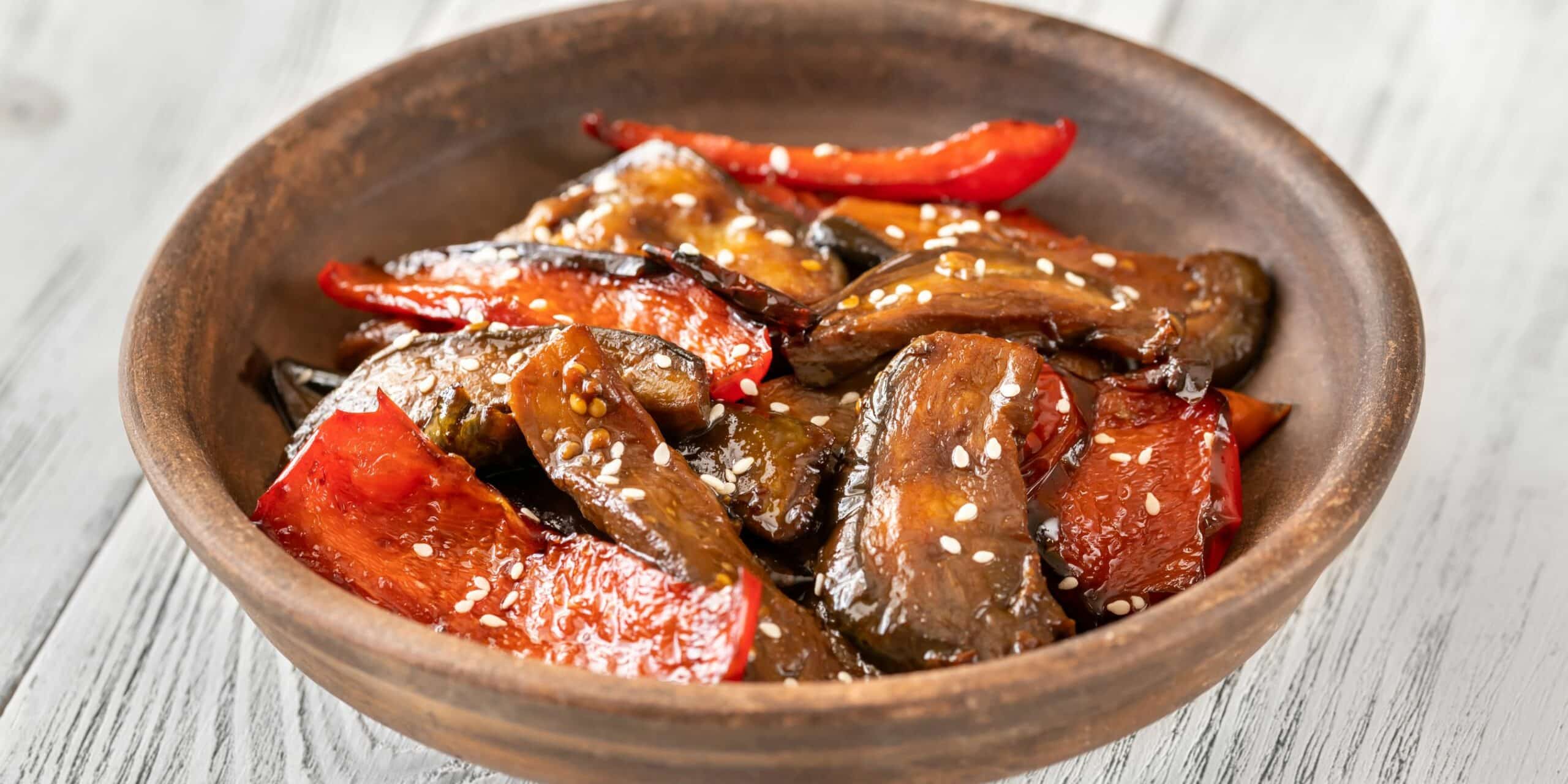 eggplant and bell pepper stir fry with sesame seeds in a brown bowl