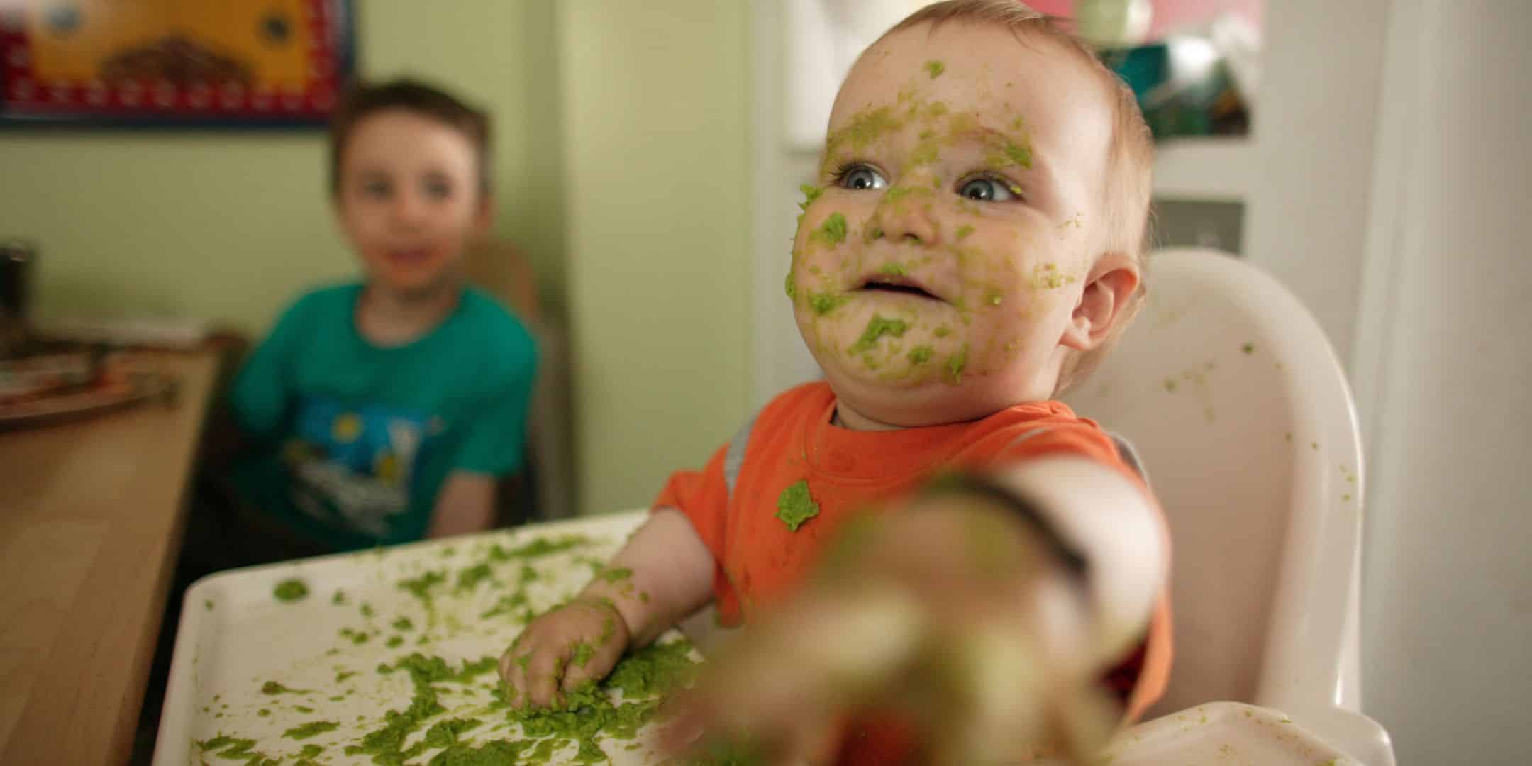baby covered in green food throwing food off the high chair