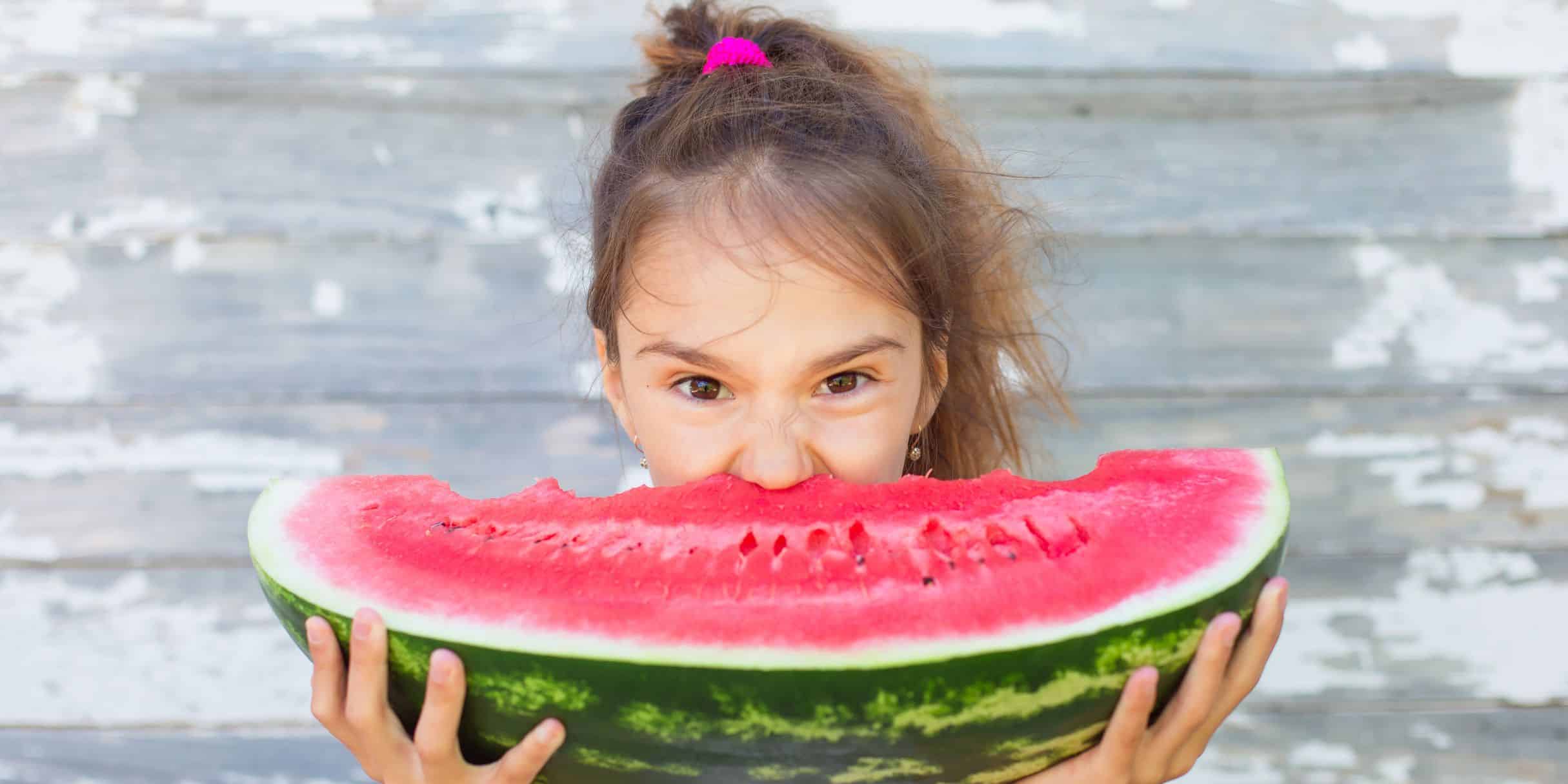 girl stuffing her mouth with a giant watermelon wedge